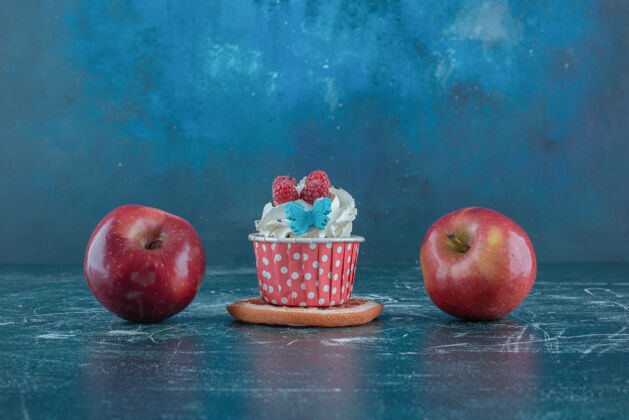 烘焙两个苹果和一个杯形蛋糕放在蓝色背景的葡萄片上高质量的照片水果甜点美味
