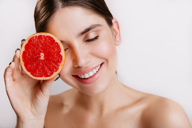微笑开朗可爱的女孩微笑着 在白色的墙上摆着红色健康的柑橘类水果活跃能量积极