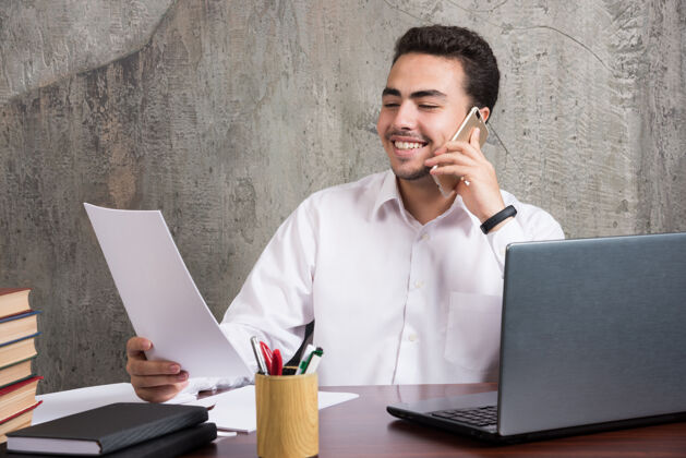 人微笑的员工在手机上交谈 拿着一张纸高质量的照片电话笔记本电脑书