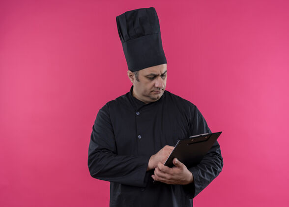 粉色男厨师身穿黑色制服 头戴厨师帽 拿着剪贴板 严肃的脸站在粉色背景上看着它厨师看严肃