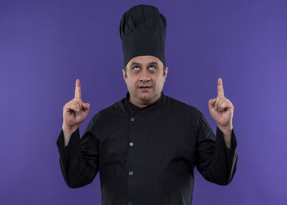紫色男厨师身穿黑色制服 头戴厨师帽 食指朝上 站在紫色背景上看穿制服