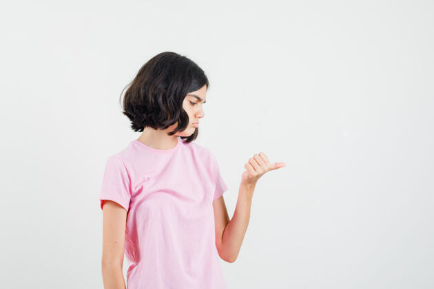 沉思小女孩展示拇指中间的粉红色t恤 看起来沉思 前视图女孩显示漂亮
