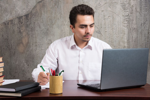 男年轻员工看着笔记本电脑 坐在办公桌前高质量的照片办公室人书