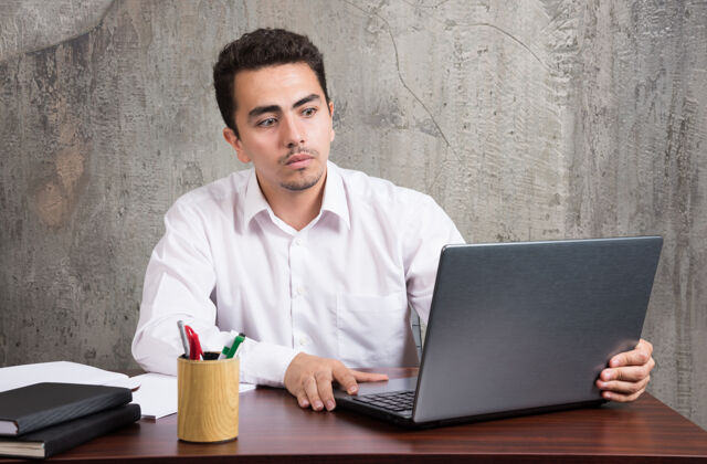 人商人看着笔记本电脑 坐在办公桌旁高质量的照片男笔记本电脑书