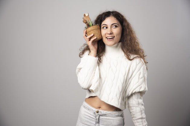 成人年轻的女园丁拿着一棵植物在灰色的墙上高质量的照片花自然女孩
