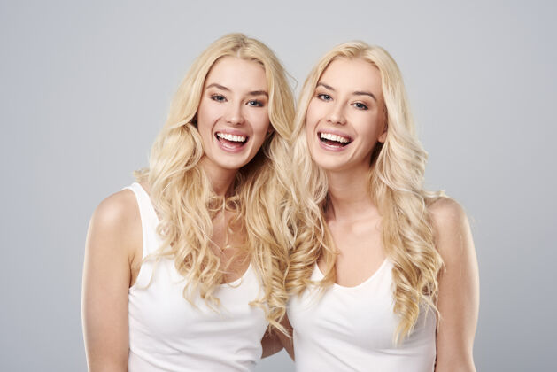欢呼在灰色背景下笑的双胞胎仅限女性比较腰部向上
