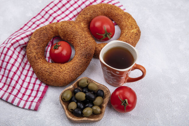 早餐白色背景上红色格子布上的木制碗上放着新鲜西红柿和橄榄的柔软土耳其百吉饼的俯视图土耳其的白的红的