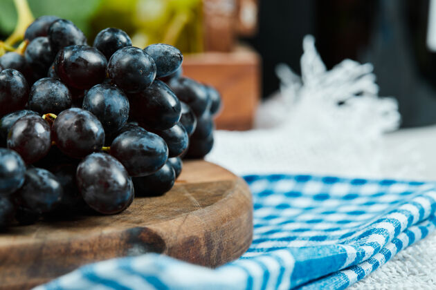 多汁用蓝色桌布在木盘上放一簇黑葡萄特写老的美味