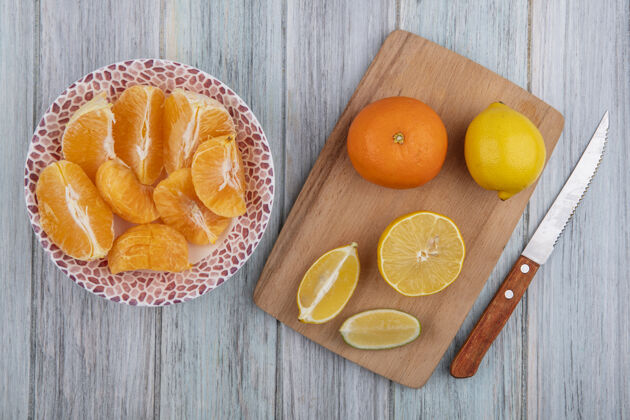灰色顶视图橙色切片与柠檬楔形板上的切纸刀在灰色背景新鲜切割食物
