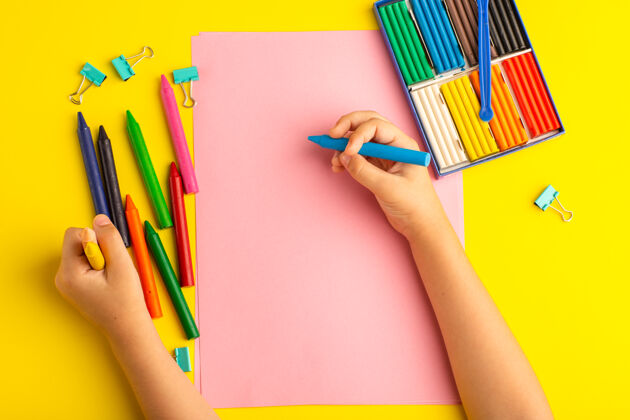 顶俯视图：小孩用彩色铅笔在黄色的粉色纸上画小钢笔孩子