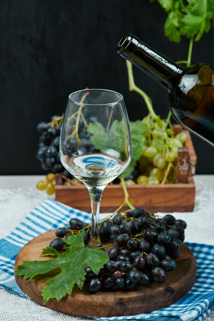 木头一盘各种葡萄和一杯葡萄酒放在白桌子上 配上酒瓶多汁手瓶子