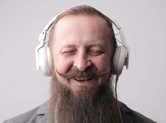 耳机一个留着长胡子 留着小胡子 戴着白色耳机的男人 站在一堵灰色的墙前成人灰色男性