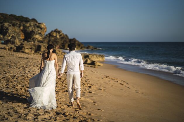 新郎新娘和新郎在沙滩上散步婚纱沙滩海滩