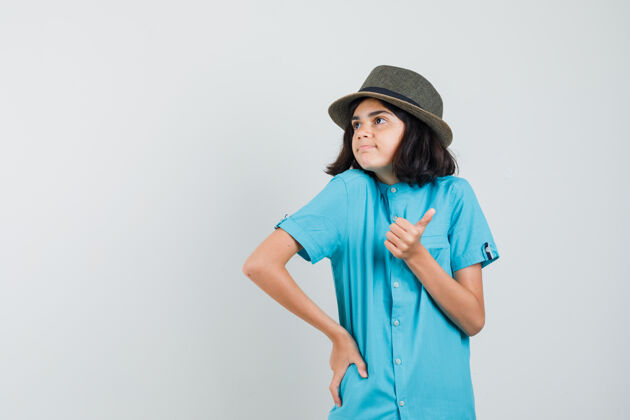 年轻穿蓝衬衫的年轻女士 戴着一顶大拇指朝上的帽子 看上去很高兴室内优雅快乐