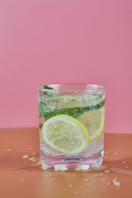 排毒一杯清凉的柠檬水放在粉红色的表面热带玻璃液体
