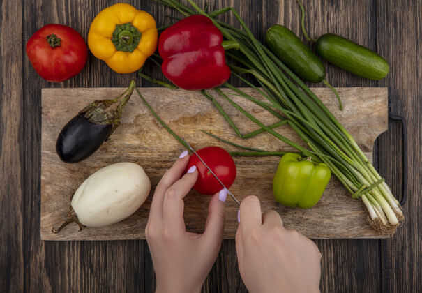 蔬菜俯视图：女人在砧板上切西红柿和葱 白色和黑色的茄子 木制背景上有彩色的甜椒绿木头午餐