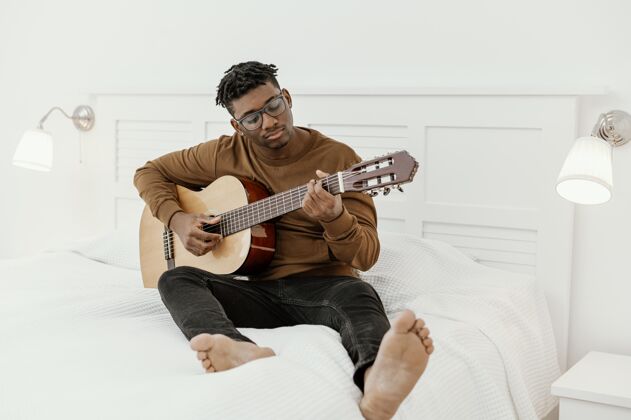 吉他男音乐家在家的正面视图 在床上弹吉他乐器手男性熟练程度