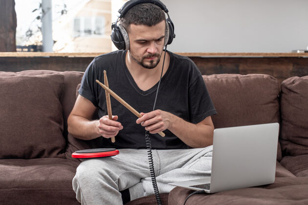 实践一个男人打鼓 看着笔记本电脑屏幕在线音乐课 视频会议课的概念远程男人音乐