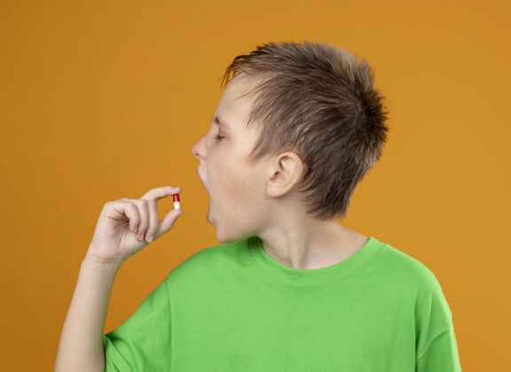 橘子生病的小男孩穿着绿色t恤 站在橘色的墙上吃着药 感觉不舒服感觉药片不舒服