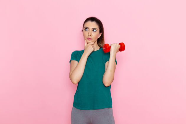 哑铃正面图年轻女性手持哑铃在粉红色的墙上运动员运动锻炼健康锻炼抱着年轻人健身