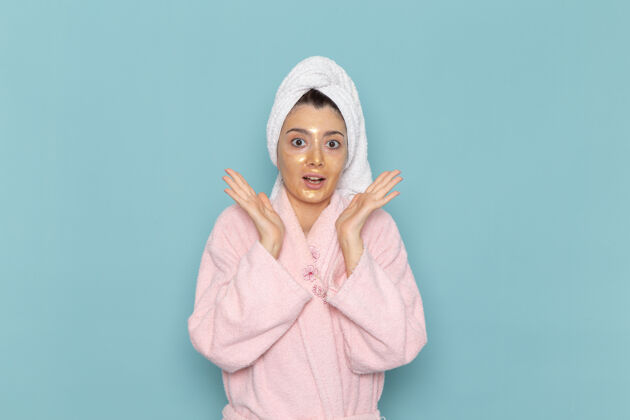 肖像正面图年轻女性穿着粉色浴袍淋浴后在浅蓝色墙壁上摆姿势美容水自理淋浴干净干净前面浅蓝色