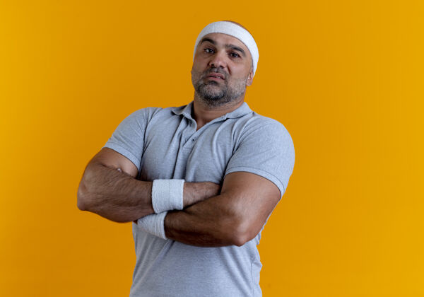 人戴着头巾的成熟运动型男子站在橙色的墙上 双手交叉放在胸前 表情严肃地看着前方教练运动运动