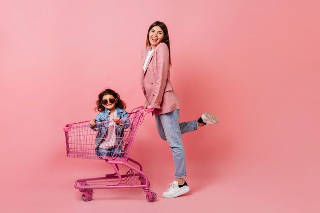 童年幸福的女人带着小女儿在购物后摆姿势微笑的母亲站在购物车旁一起人牛仔裤