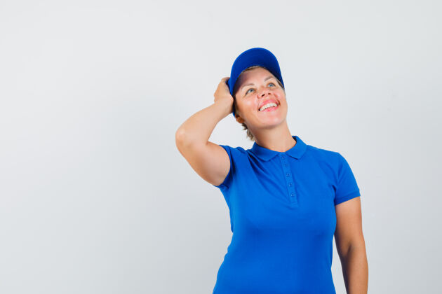 可爱一个穿着蓝色t恤的成熟女人 手举在头上 看起来很梦幻帽子看起来自信