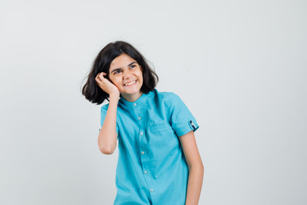 表情一个十几岁的女孩手放在脸颊上 穿着蓝色衬衫微笑着 看上去很高兴时尚青少年人