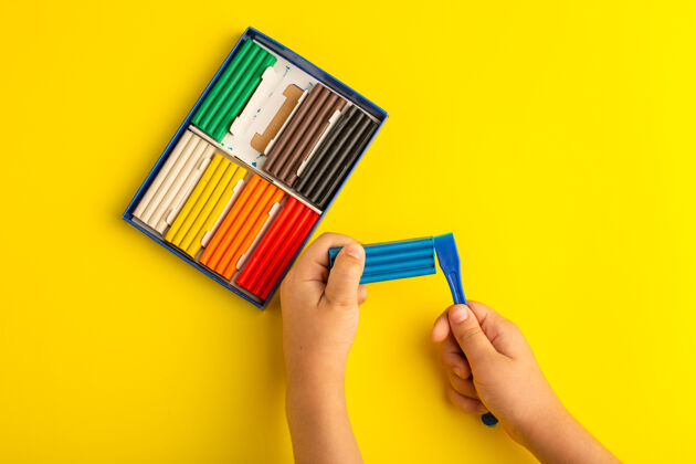 购物者顶视图彩色橡皮泥儿童工作和玩它的黄色墙上彩色照片儿童学校持有彩色画笔
