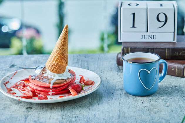杯子在日历和书的表面放上薄饼和冰淇淋筒 草莓和热茶草莓煎饼数字