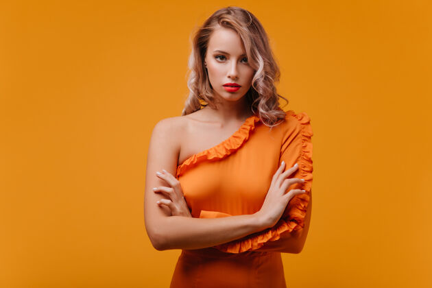 乐趣对时尚橙色连衣裙感兴趣的女人交叉双臂摆姿势人服饰明亮