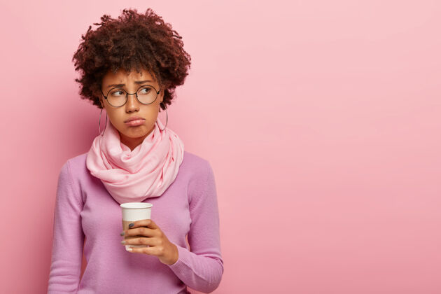 一次性摄影棚拍摄的不高兴的黑皮肤女性喝新鲜咖啡作为早晨的点心围巾杯子美式