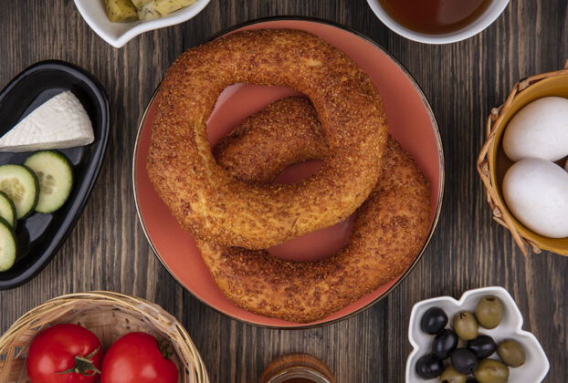 桶土耳其芝麻百吉饼的顶视图 盘子里放着橄榄 桶里放着西红柿 背景是木制的食物木头小吃