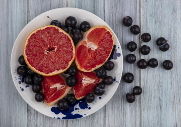 李子俯视图：灰色背景的盘子上放着一半的葡萄柚和樱桃李子葡萄柚一半樱桃色