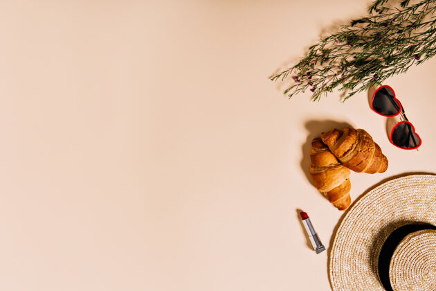 腮红野餐的羊角包 帽子 眼镜和可爱的小花躺在米色的墙上纸袋野餐美容
