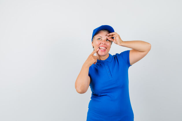 成熟穿蓝色t恤的成熟女人 露出ok标志 伸出舌头 看起来很快乐自信姿势帽子