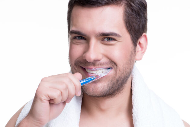 站立一个快乐的年轻人在白墙上刷牙的特写照片牙齿成人没刮胡子