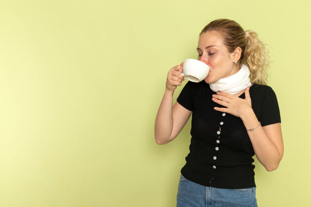 疾病正面图年轻女性感觉很不舒服 在绿墙上抱着一杯咖啡喝着病药病健康持有病人音响设备