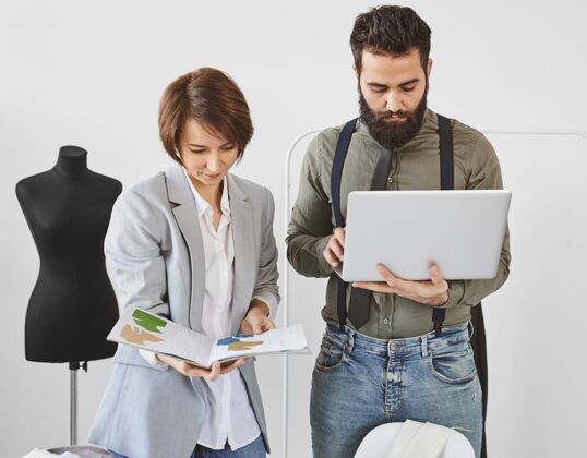 创意两位时装设计师在工作室里用笔记本电脑工作的前视图个人服装师水平