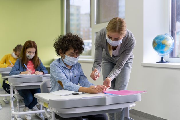 孩子带着医用口罩的女老师在教室里给孩子们洗手新常态学校课堂