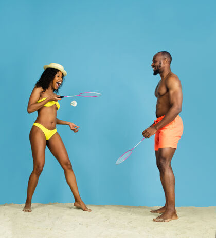 太阳镜最疯狂的乐趣快乐的年轻的非洲裔美国夫妇打羽毛球在蓝色的工作室背景人类情感的概念 面部表情 暑假或周末寒冷 夏天 海洋巴塞罗那霓虹灯冷