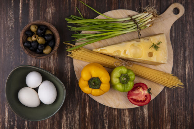 马斯丹顶视图：鸡蛋放在碗里 橄榄 葱 甜椒 马斯坦奶酪片和番茄放在木制背景上切片视图绿色