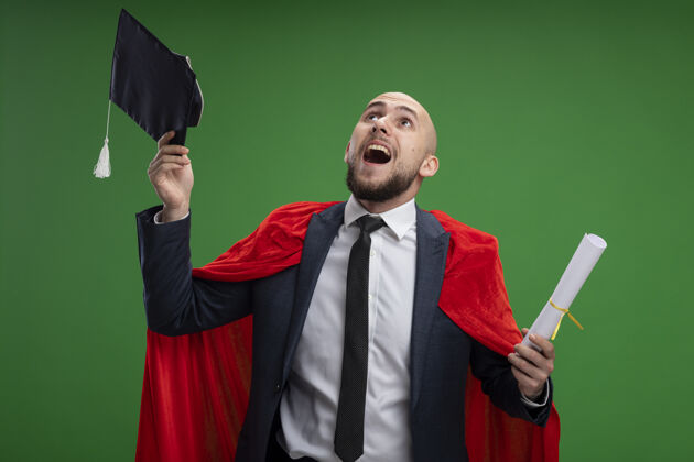 证书毕业的红衣人拿着毕业证书 高高兴兴地扔着帽子站在绿色的墙上毕业立场斗篷