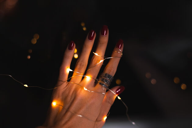指甲美丽的黑色照片的妇女手指头与大银戒指上的花朵和发光的灯光手明亮样品