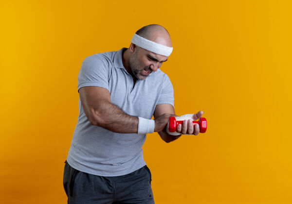 人戴着头巾的成熟的运动型男人站在橘色的墙上 摸着他缠着绷带的手 看起来很不舒服成熟人头带