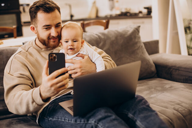 父母年轻的父亲和他的女婴坐在一起 在家里用电脑可爱的女孩沙发小玩意