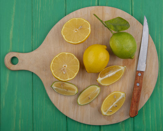 水果顶视图柠檬片和一把刀在一个绿色背景的砧板上绿色柠檬刀