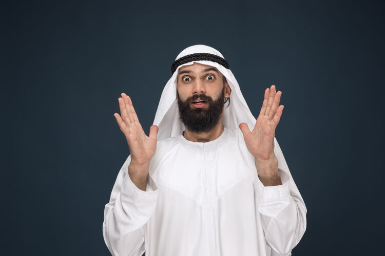 发呆深蓝色工作室背景上的阿拉伯沙特商人肖像年轻的男模站着震惊和惊讶商业概念 金融 面部表情 人类情感呼叫沙特