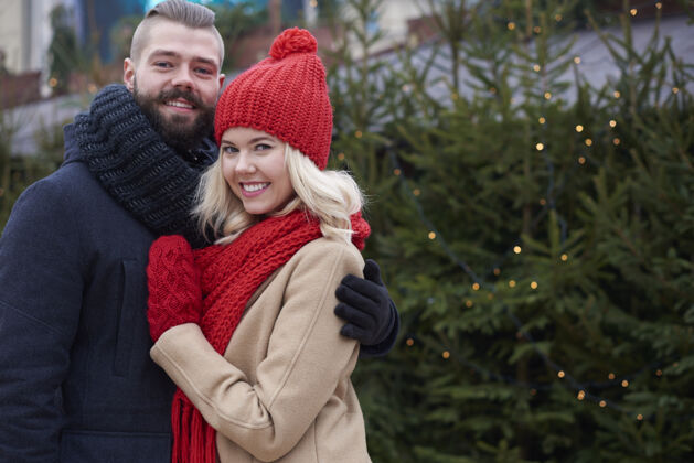 围巾在圣诞树旁拥抱的情侣帽子肖像微笑